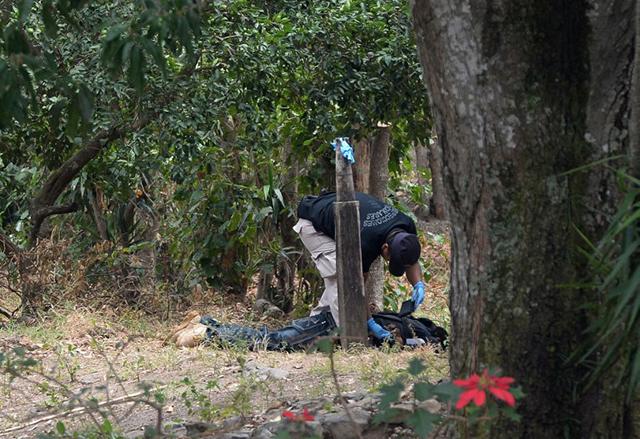 Un agente del equipo de Inspecciones Oculares de la Policía Nacional Civil revisa el cadáver de José Antonio Gómez, alias Güereja, en la mañana del 26 de marzo. El médico forense que reconoció el cuerpo contabilizó 23 orificios de bala. Foto Marvin Recinos (AFP).